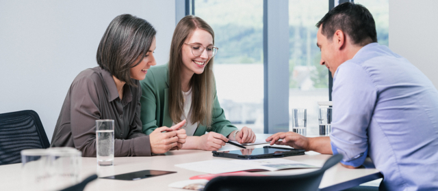 Drei Personen arbeiten konzentriert am Tisch mit einem Tablet.